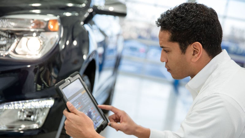 A technician reviewing an ipad while inspecting a car 